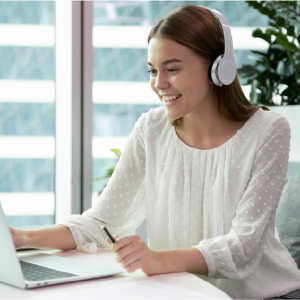 A smiling woman wearing white headphones works at her laptop