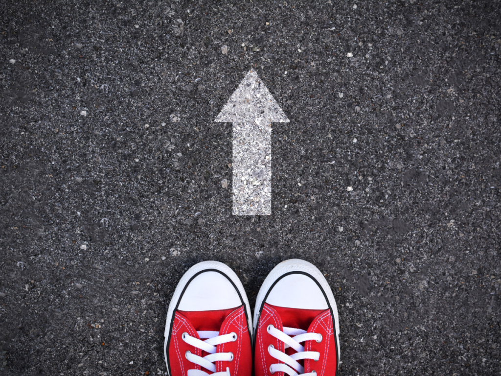 Sneakers on a bitumen road point in the same direction as an arrow that is painted on the road