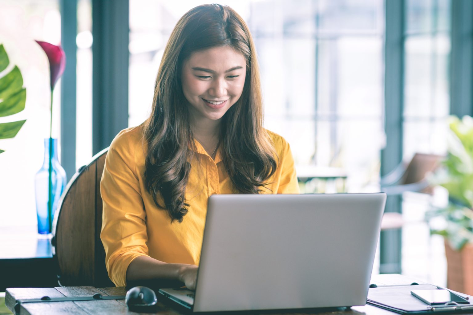 A woman in a yellow shirt smiles as she works at a laptop