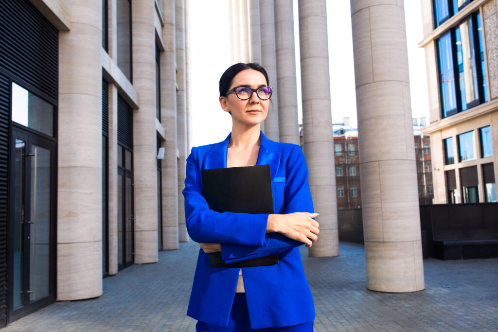 A businesswoman stands outside a government office holding a folder of briefs