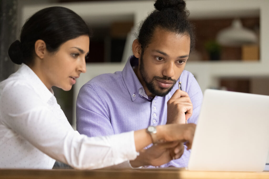 Two colleagues review a document on a laptop - one colleague points to the screen while the other looks closely