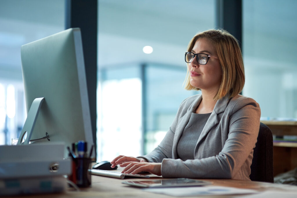 A businesswoman sits at her computer in her office writing letters and emails