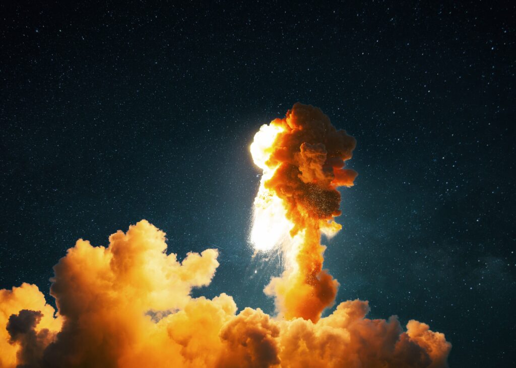 A rocket explodes leaving an orange plume of smoke in the night sky.