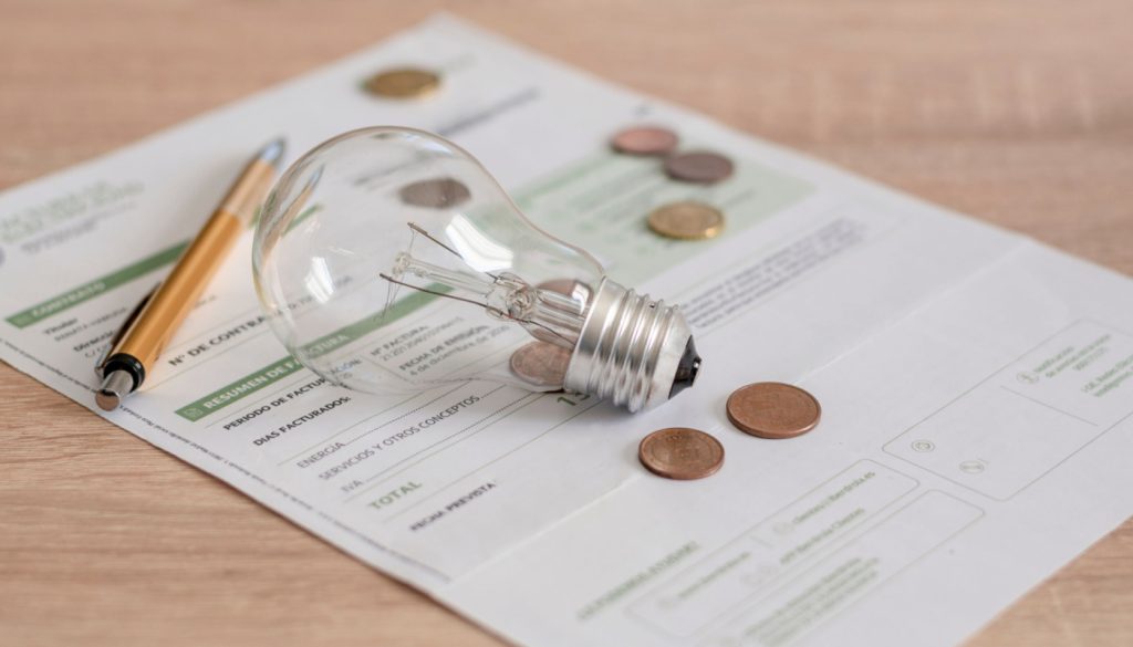 A pen, a lightbulb and some coins sit on top of the bill.