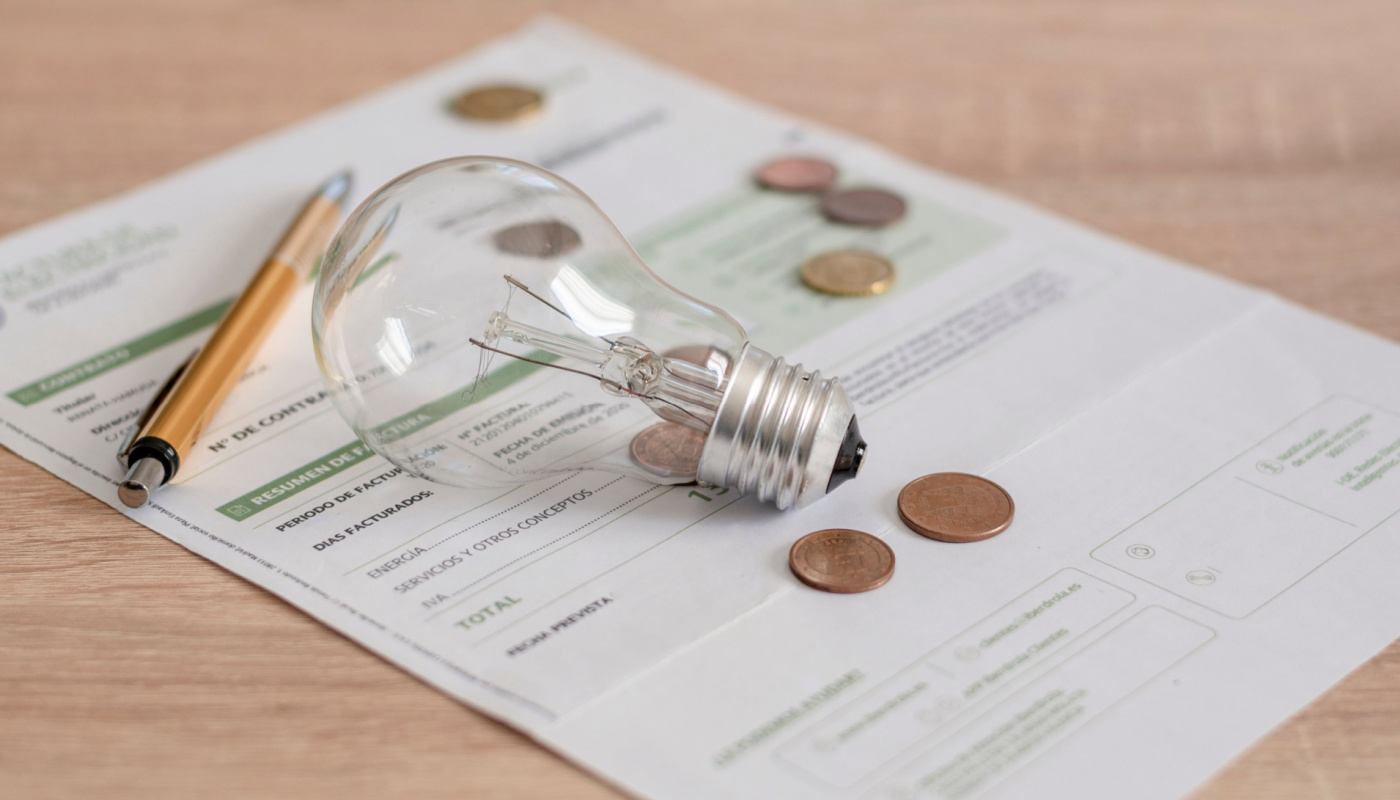 A pen, a lightbulb and some coins sit on top of the bill.