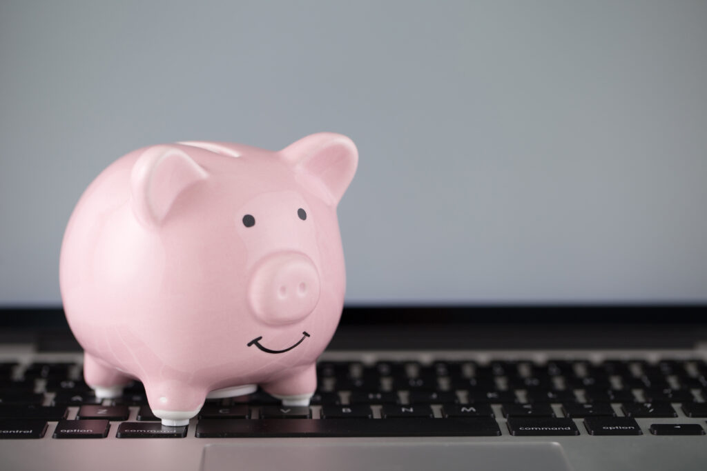 A piggy bank sits on the keyboard of a laptop.
