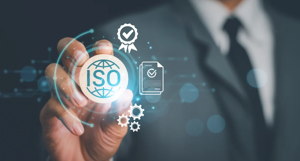 Fingers tweak an ISO icon. Other icons surround it: a certification ribbon, a ticked document and cogs.