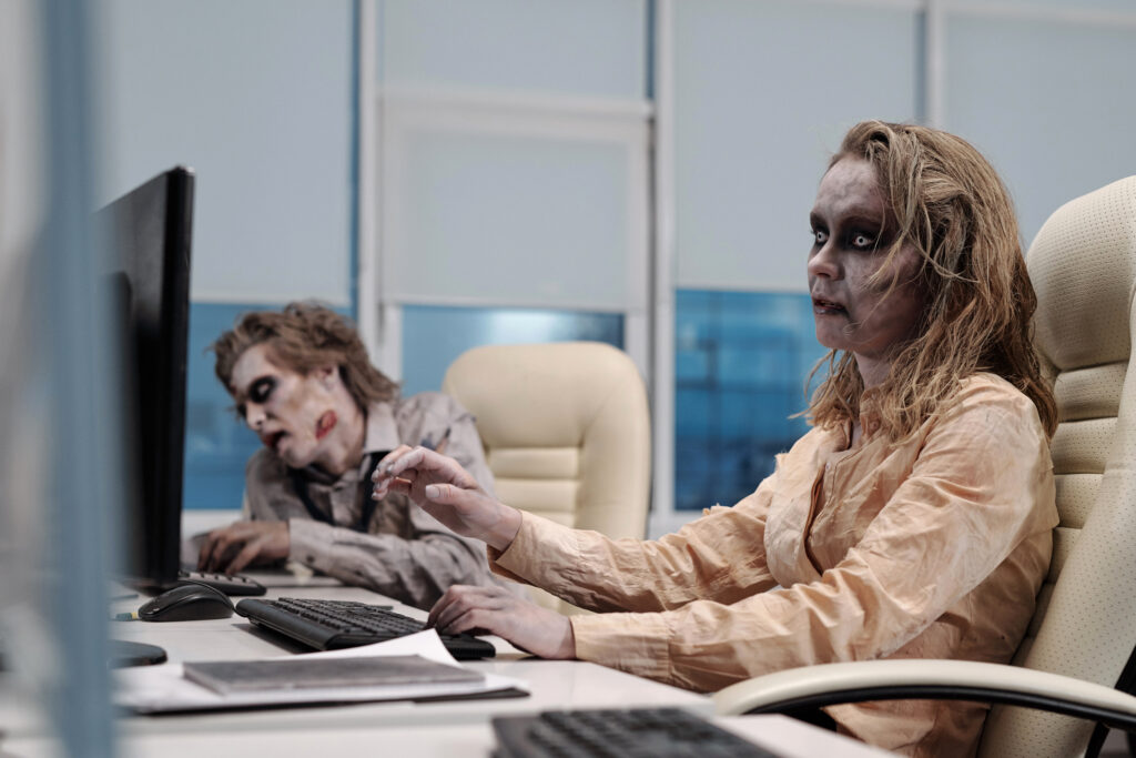Two zombies work at computers in an office setting.
